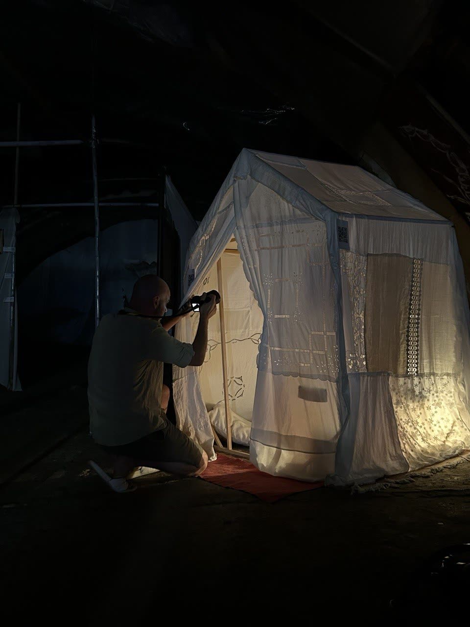 A photographer kneeling to shoot the glowing textile house in the dark